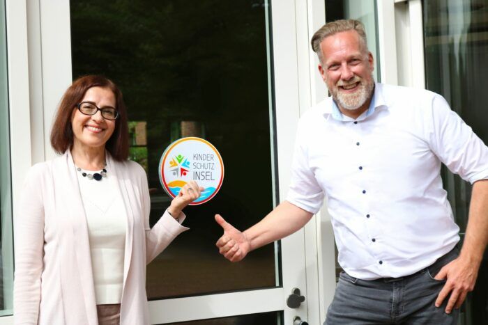 Natalia Kontour-Selivanov und Ingo Mahl zeigen das Logo der Kinderschutzinsel am Eingang der Schlüterschen